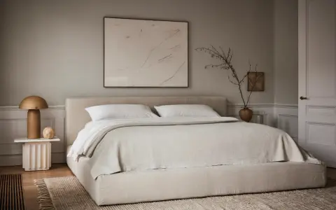Une chambre beige apaisante avec un lit bas, une table de chevet sculpturale et une œuvre d'art abstraite.