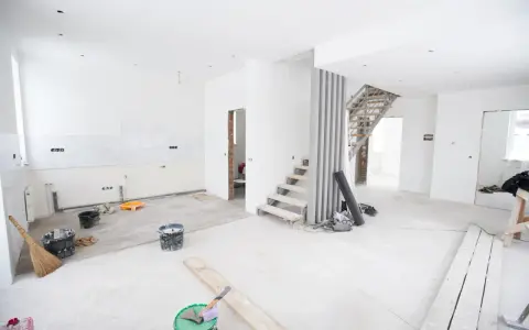 Chantier en cours pour rénover ma maison : escalier, seaux de peinture, balai et matériaux au sol.