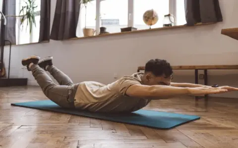 Homme faisant un exercice dos sur un tapis, bras tendus, jambes levées.
