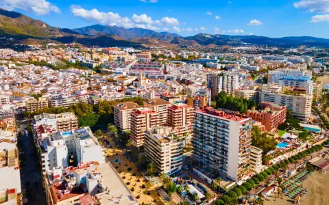 Widok z lotu ptaka na nadmorskie miasto Marbella, z górami w tle. Widać plażę, hotele i budynki mieszkalne.