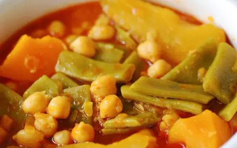 Un plato humeante de olla gitana, con garbanzos tiernos, judías verdes y trozos de calabaza en un rico caldo.