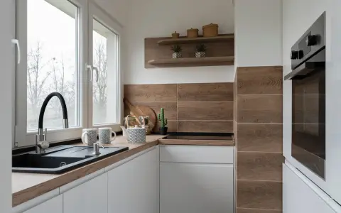 Mała kuchnia inspiracje: białe szafki, drewniany blat i płytki, czarny zlew, ozdoby na półce.