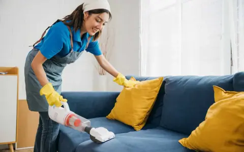 Femme nettoyant un canapé bleu avec un aspirateur pour éliminer la mauvaise odeur du tissu.