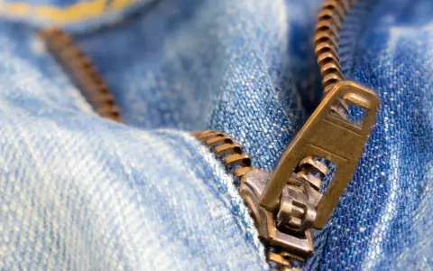 Nahaufnahme eines Reißverschlusses an Jeans. Der Schieber ist halb geöffnet. Ein guter Zeitpunkt, um den Reißverschluss reparieren zu lassen.