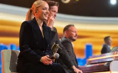 Uśmiechnięta wokalistka, która śpiewa w "Jaka to melodia", siedzi obok pianistów na scenie.