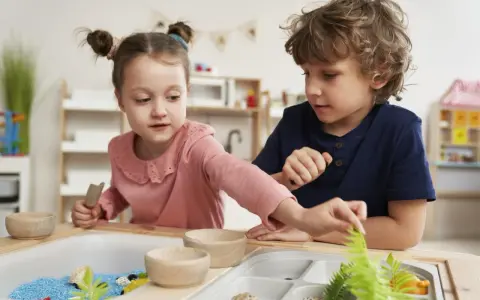 Dwoje dzieci bawi się w piaskownicy sensorycznej z niebieskim piaskiem i roślinami.