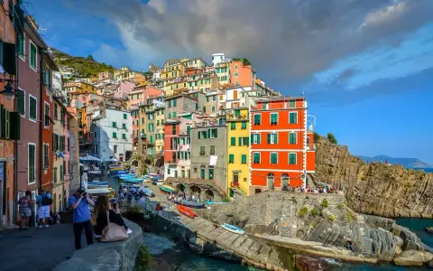 Bunte Häuserfronten der Cinque Terre Orte schmiegen sich an steile Felsen. Boote liegen im türkisfarbenen Wasser.
