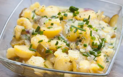 Kartoffelsalat ohne Mayo, mit Gurken, Zwiebeln und Schnittlauch in einer Glasschüssel.