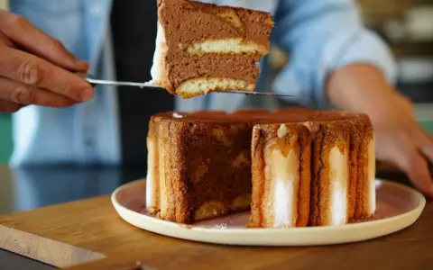 Une part de charlotte tiramisu, aérienne et chocolatée, est prélevée d'un gâteau entier.