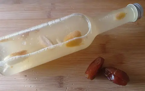 Flasche mit Flüssigkeit und Fruchtstücken, bereit zum Hefe selber machen. Daneben liegen zwei Datteln.