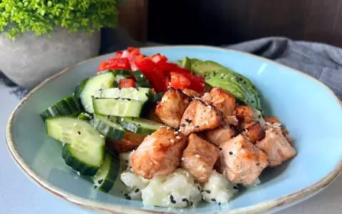 Pyszny bowl z kawałkami pieczonego lososia, świeżym ogórkiem, pomidorem i awokado na ryżu.