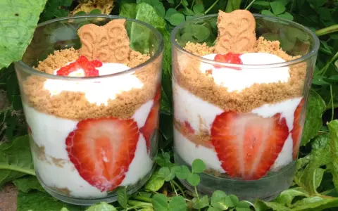 Deux verrines de tiramisu fraises spéculoos, garnies de crème, fraises fraîches et biscuits spéculoos, posées sur un lit de verdure.
