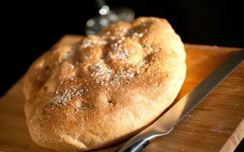 Focaccia rustica con sale grosso e rosmarino, pronta per essere tagliata. Un invito a gustare, come il pan per focaccia significato.