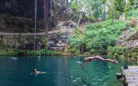 Una ragazza si tuffa nel **cenote Zaci**, un'oasi naturale con acque cristalline e vegetazione lussureggiante.