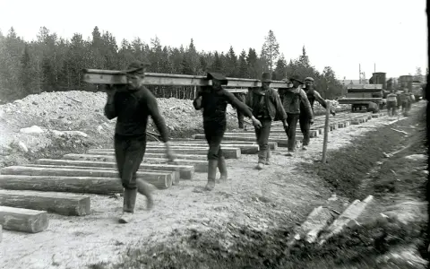 Rallarna i Sverige bär tunga stockar för järnvägsbygge.