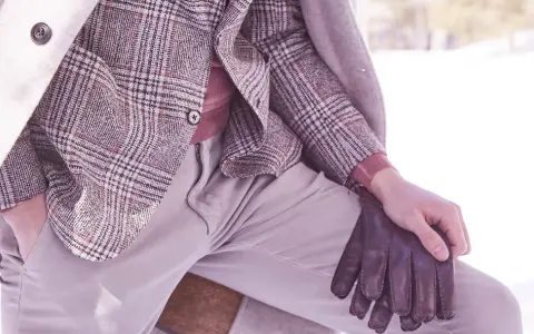 Un uomo indossa un elegante spezzato con giacca a quadri, maglione rosa e guanti in pelle marrone, pronto per l'inverno.