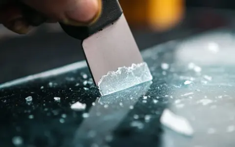 A scraper is used to remove adhesive from acrylic, leaving behind small white fragments.