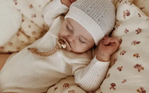 Śpiące dziecko w czapce i pajacyku z wełny merino. Czy wełna merino gryzie? Nie, jest miękka i delikatna dla skóry maluszka.