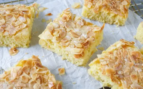 Saftiger Buttermilch Kuchen mit knusprigen Mandelblättchen und Zucker bestreut, auf Backpapier und einem Gitterrost arrangiert.