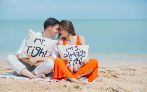 Para zakochanych na plaży z poduszkami "Mr. Right" i "Mrs. Always Right". Ich uśmiechy i bliskość symbolizują idealny **kompromis w związku**.