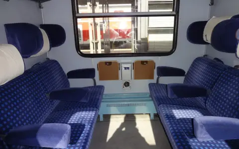 Wnętrze wagonu z niebieskimi siedzeniami w kratkę. Różne rodzaje wagonów oferują komfort podróży.