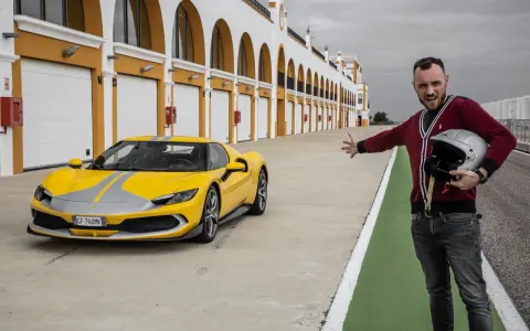 Żółte Ferrari 296 GTB z szarymi pasami na torze wyścigowym. Obok stoi mężczyzna z kaskiem, zapraszając do przejażdżki.