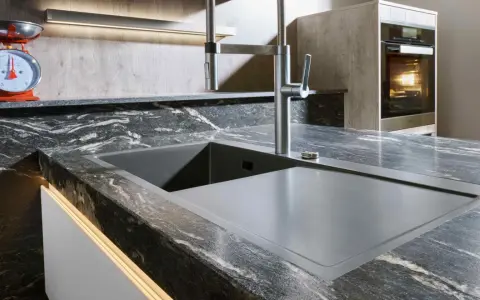 Moderne Küche mit Spüle und Armatur auf einer dunklen Keramik-Arbeitsplatte. Vorsicht vor Bruchgefahr bei unsachgemäßer Handhabung.