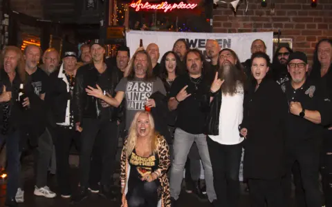 En grupp glada musiker, redo för swedish metal aid. En kvinna i leopardmönstrat poserar i förgrunden.