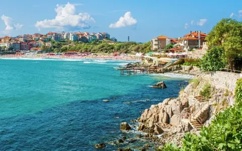 Widok na bułgarskie wybrzeże z kamienistymi klifami, plażą i zabudowaniami. Czy w Bułgarii są palmy? Tak, w niektórych miejscach można je spotkać.