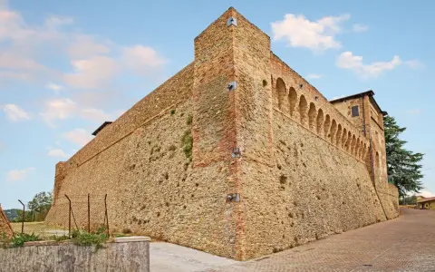 Antica fortezza nella valle del Rubicone, con mura in pietra e mattoni, torri e un loggiato ad archi.