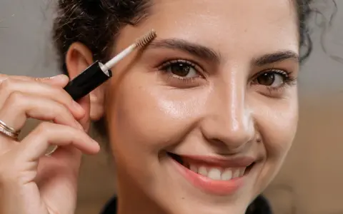 Une femme souriante utilise une brosse pour redessiner ses sourcils.