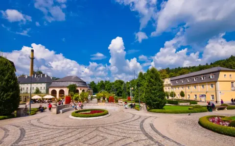 Słoneczny dzień w Kudowie Zdrój. Spacerowicze odpoczywają w pięknym parku zdrojowym, otoczonym zabytkową architekturą.