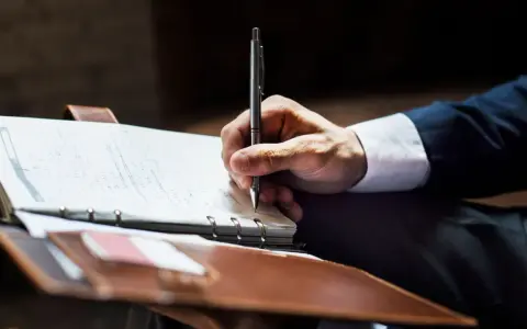 Mężczyzna w garniturze pisze w notatniku. Może to być wzór wniosku o umorzenie długu u komornika.