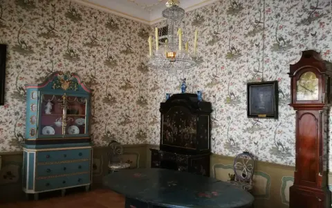 Wnętrze Uphagen House: zabytkowy zegar, szafka, stół i tapeta z ptakami.
