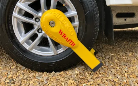 Żółte zabezpieczenie przyczepy kempingowej Milenco Wraith na feldze koła, zapewniające bezpieczeństwo podczas postoju.