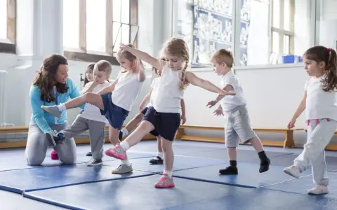 Niños aprendiendo movimientos de **deportes para niños** con una maestra en un gimnasio.