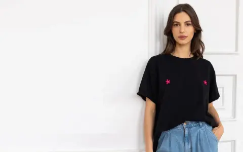 Kobieta w czarnym t-shircie z haftowanymi kwiatkami i jeansach. Stylowy sposób, jak nosić t-shirt w spodniach.