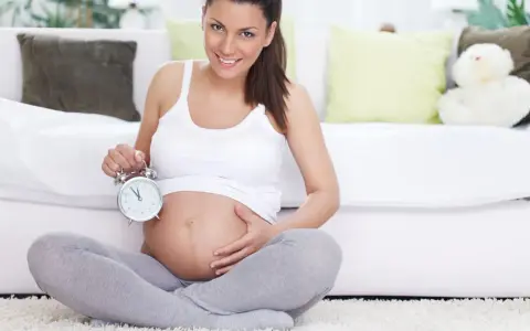 Uśmiechnięta kobieta w 40 tygodniu ciąży trzyma budzik. Czas na poród!