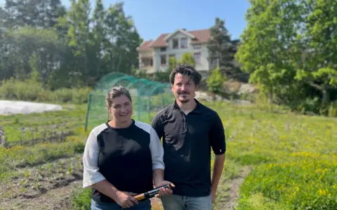 Två personer står på en åker vid Peters place Grebbestad. Bakom dem syns ett hus och grönskande träd.