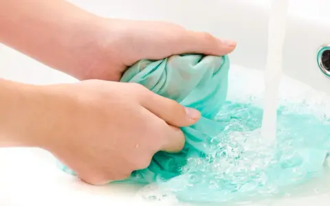 Hände waschen ein türkises Tuch im Waschbecken, um Fettflecken zu entfernen. Wasser sprudelt und schäumt.