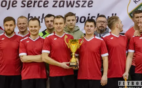 Drużyna w czerwonych koszulkach świętuje zwycięstwo z pucharem. W centrum stoi Andrzej Zaborowski, dumny z sukcesu.