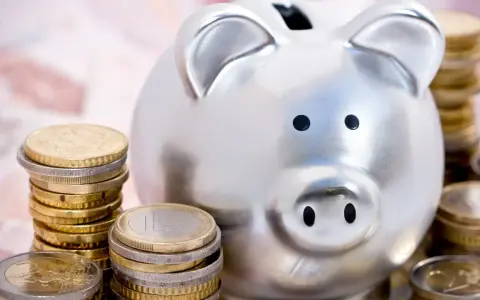 Hucha plateada rodeada de pilas de monedas de euro, simbolizando las ventajas del euro para el ahorro.