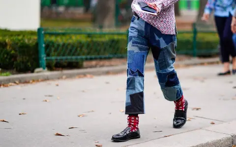 Uomo con jeans patchwork e mocassini neri, calzini rossi a fantasia.