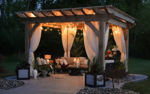 Mysig altan med pergola, draperade gardiner och stämningsfull belysning. Perfekt inspiration för din egen altanbelysning.