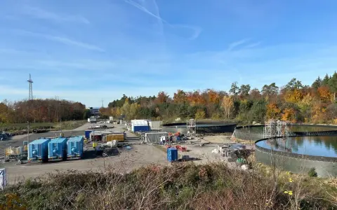 Baustelle mit großen Wasserbehältern und blauen Containern. Hier wird gezeigt, wie funktioniert geothermie mit Erdwärme.