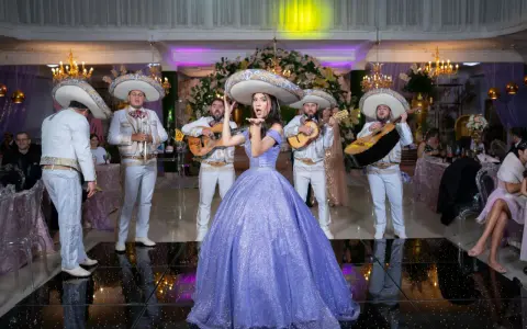 Mariachi grają, a dziewczyna w fioletowej sukni posyła całusy. W tle weselne dekoracje i goście. Idealna sceneria do przyśpiewki weselne tekst.
