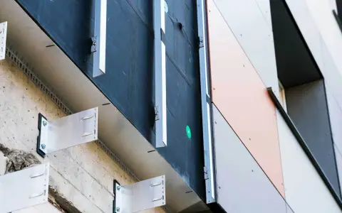 System mocowania elewacji wentylowanej. Metalowe wsporniki przytwierdzone do betonowej ściany, tworzące przestrzeń dla izolacji i wentylacji.