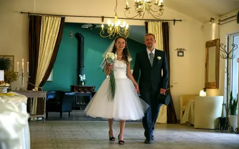 Para młoda idzie ręka w rękę. Panna młoda w sukni w stylu retro, pan młody z cylindrem. Wesele w stylu retro.
