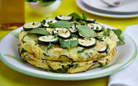 Deliciosa tortilla de calabacín y espinacas, coronada con rodajas de calabacín y hierbas frescas.