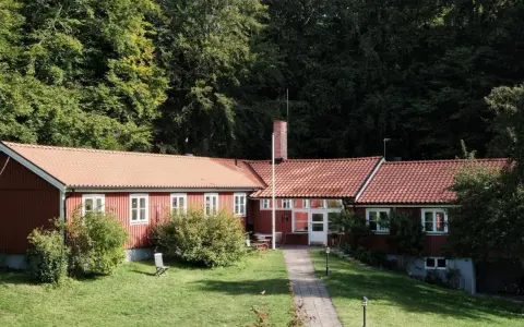 Stocklycke vandrarhem, ett rött hus med tegeltak, omgivet av grönskande träd och en välskött gräsmatta.